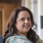 Headshot of Yvette Montero Salvatico, a woman with light skin and shoulder-length, dark brown hair, smiling warmly. They are wearing a patterned top with soft tones, and the background suggests an indoor setting with natural light coming through windows. The individual’s expression is friendly and approachable, contributing to the overall relaxed and inviting atmosphere of the image.