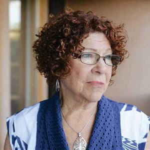 This image features a woman, identified as Margaret J. Wheatley, looking contemplatively to the side. She has light skin, curly red hair, wears glasses, and is dressed in a blue and white top with a pendant necklace. The setting appears to be indoors with a soft, neutral background.