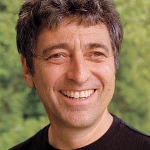 Headshot of Robert Gass, a man with light skin, short dark hair, and a bright smile. They are wearing a dark, plain shirt and are posed outdoors, with greenery visible in the background. The individual's expression is cheerful and relaxed, and the natural setting adds a fresh, lively feel to the image.